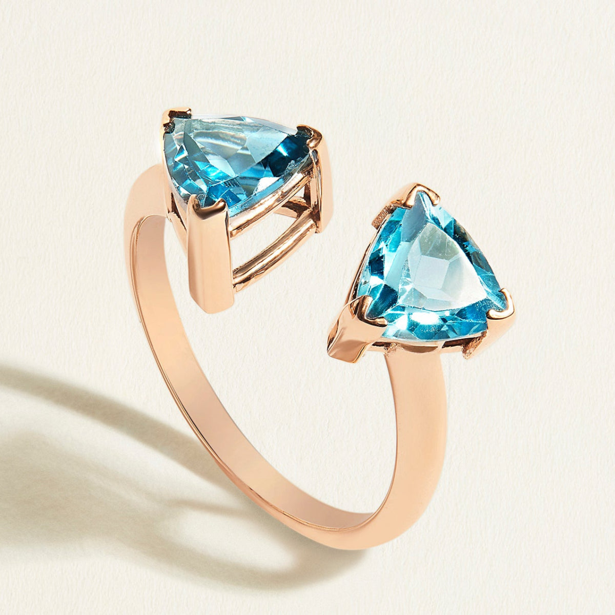 Rose gold ring toi et moi  with swiss blue and london blue topaz gemstones on a light beige background