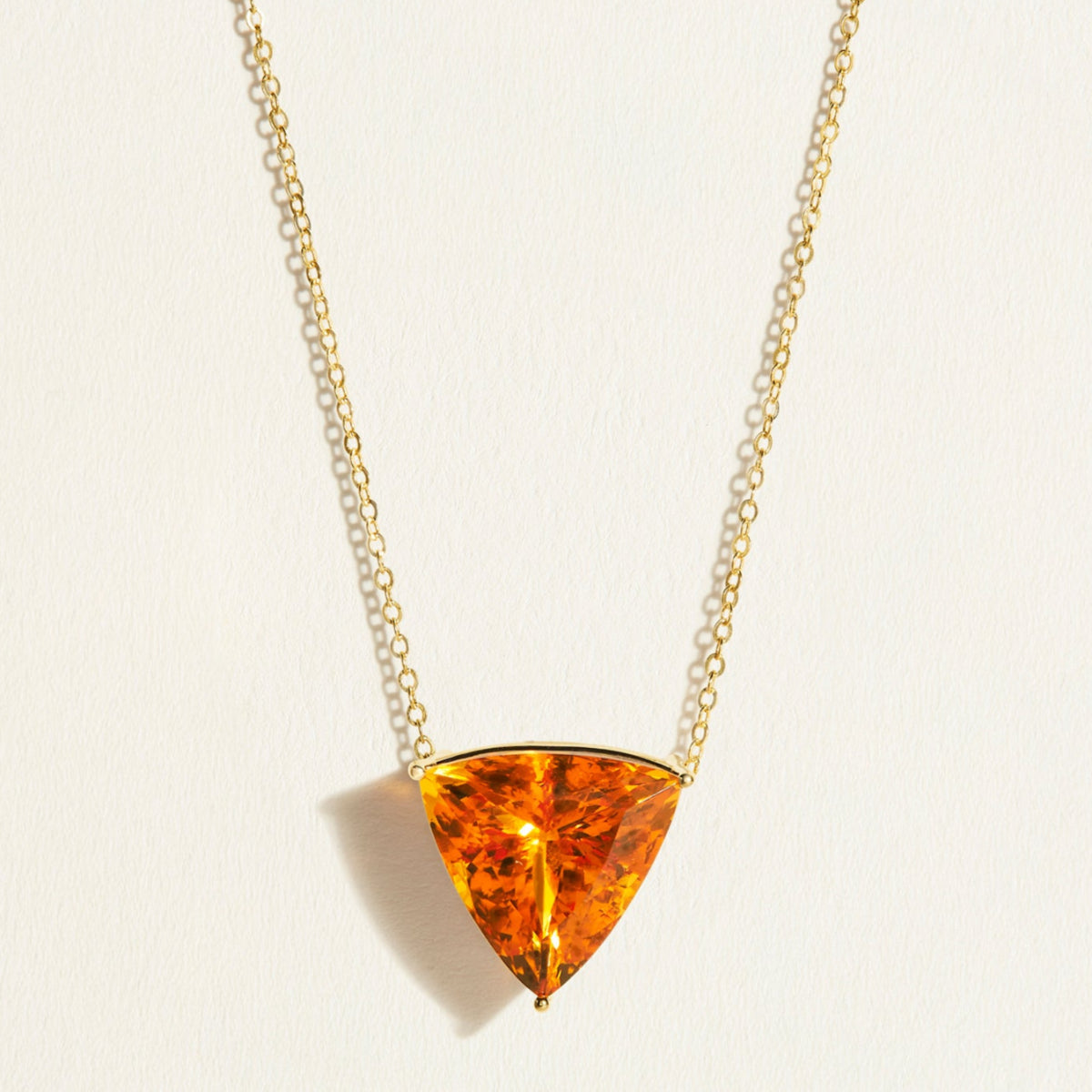 14 k Gold chain necklace with a large triangular amber  orange yellow citrine pendant on a light background