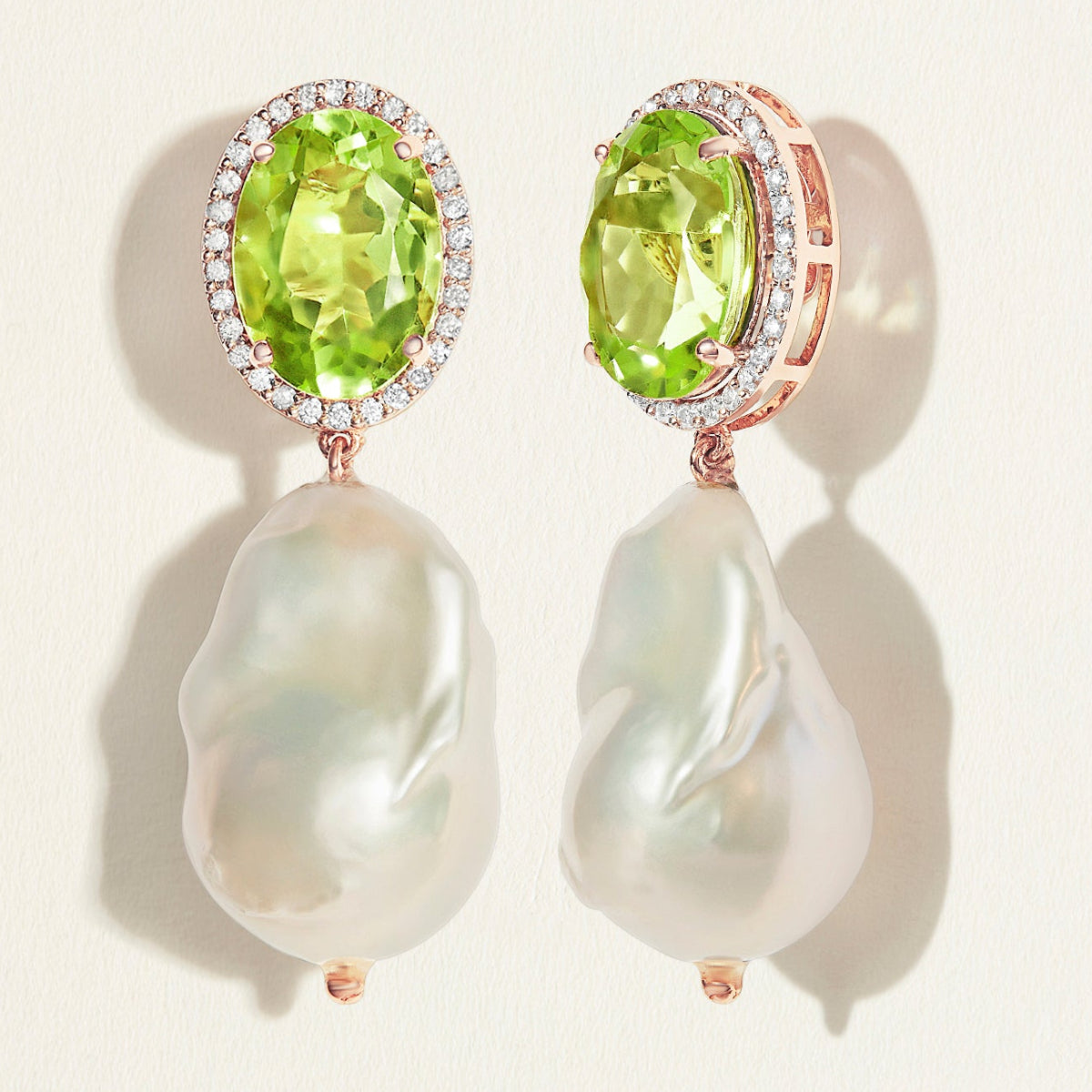 Pair of earrings with oval green peridot gemstones with diamond halo  and  baroque pearl drops on a light background