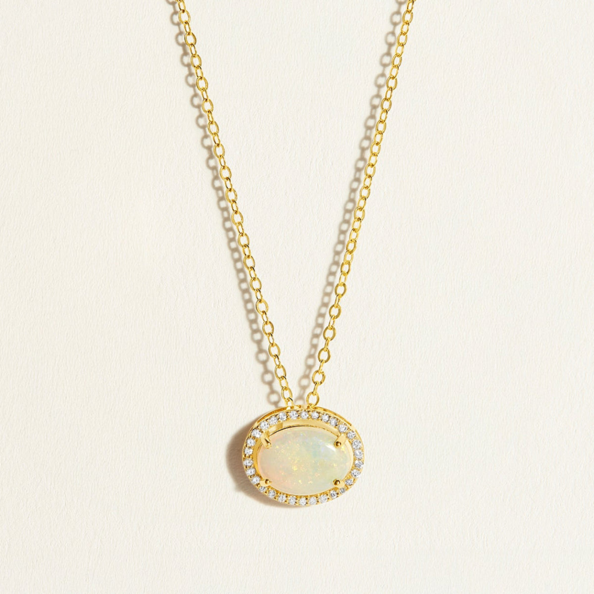 14k Gold everyday chain necklace with an opal pendant with diamond halo on a light beige background