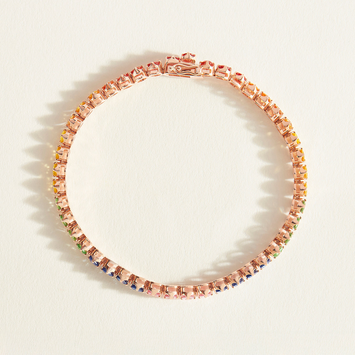 Rose gold tennis bracelet with rainbow sapphire stones on a white background