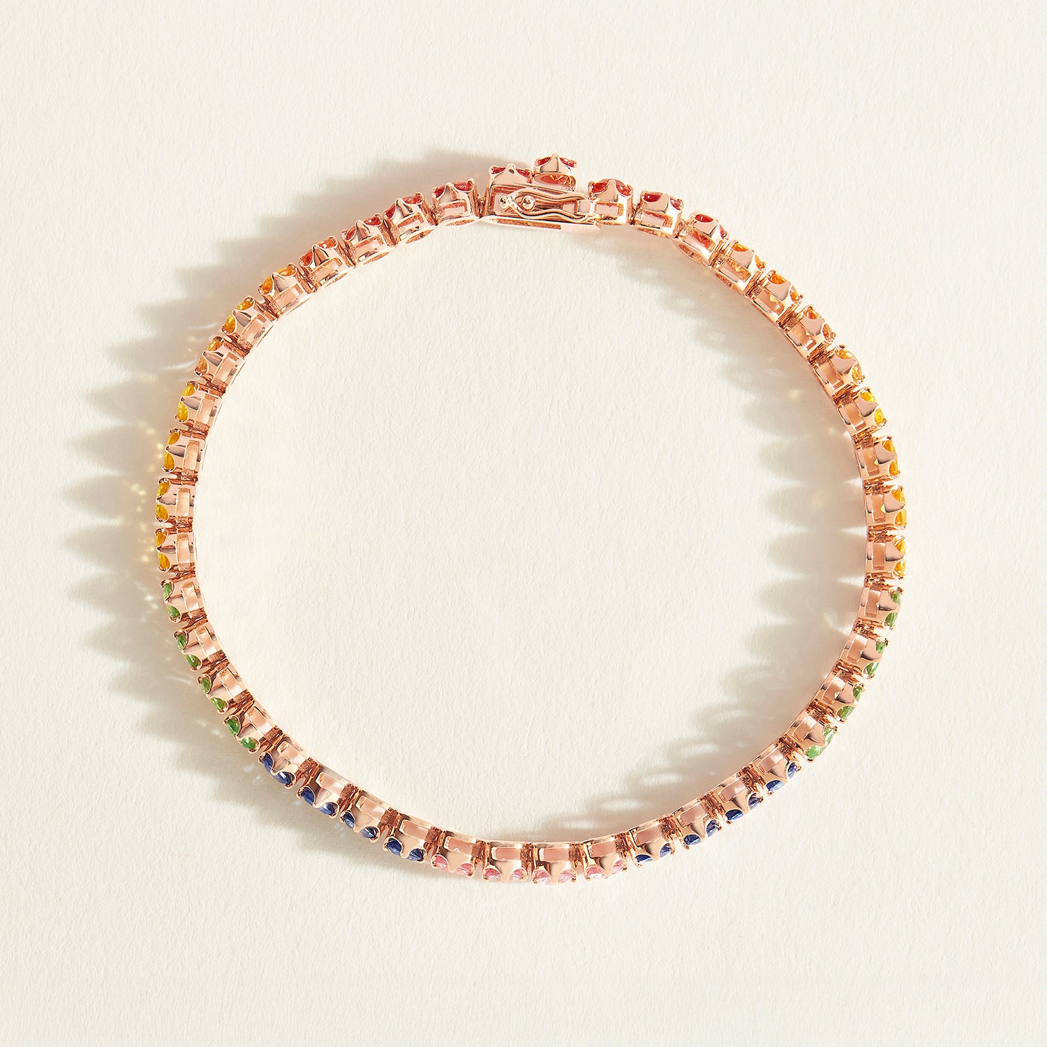 Rose gold tennis bracelet with rainbow sapphire stones on a white background