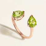 Rose gold toi et moi ring with two green pear-shaped peridot gemstones on a light background