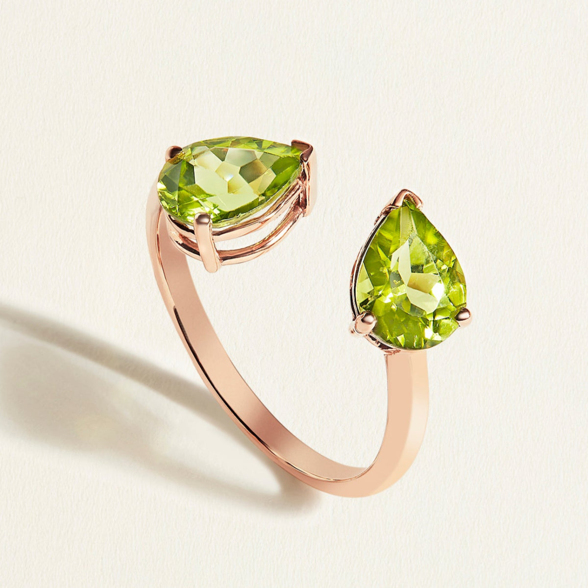 Rose gold toi et moi ring with two green pear-shaped peridot gemstones on a light background