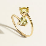 18 k Gold ring with two green amethyst trillion  gemstones on a light beige background