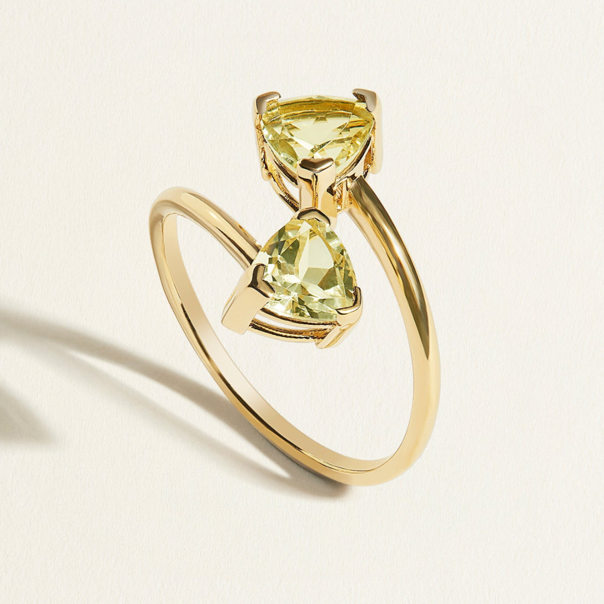 18 k Gold ring with two green amethyst trillion  gemstones on a light beige background