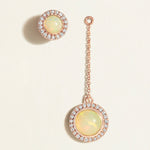 Pair of opal earrings with rose gold chains on a light beige background