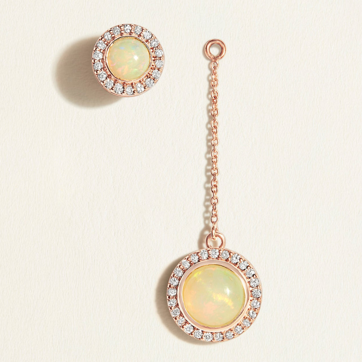 Pair of opal earrings with rose gold chains on a light beige background