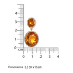 Bold Gold earrings with orange gemstones and a ruler for scale on a white background