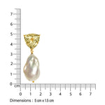 Gold designer earring with a light green  gemstone and baroque pearl, measured against a ruler on a white background.