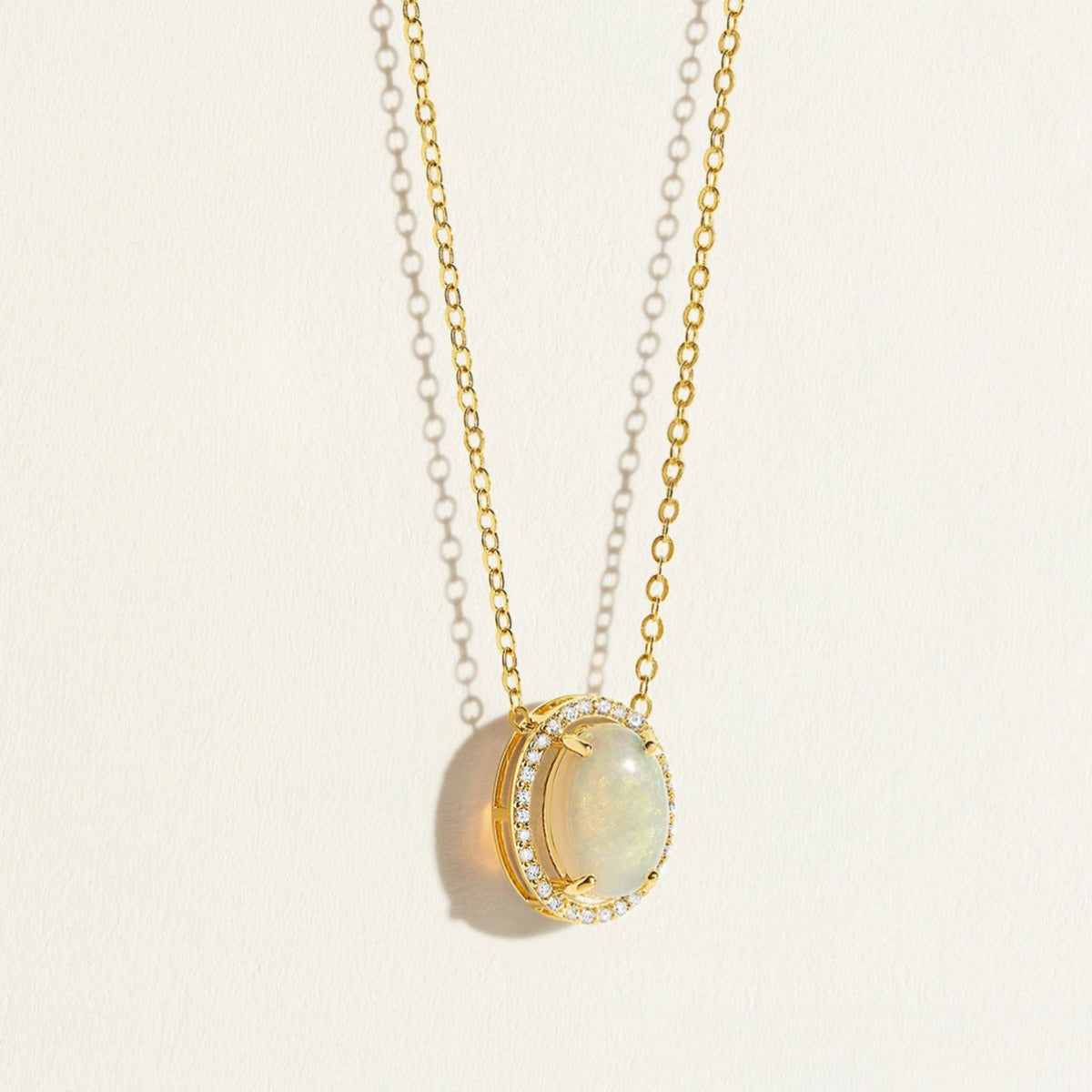 14k Gold everyday chain necklace with an opal pendant with diamond halo on a light beige background
