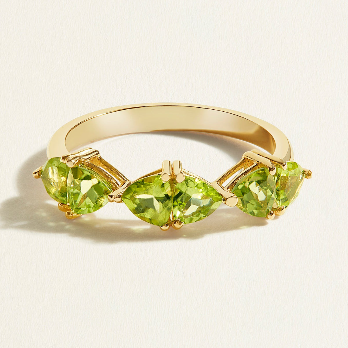 Gold stacking ring with green peridot gemstones on a light beige background