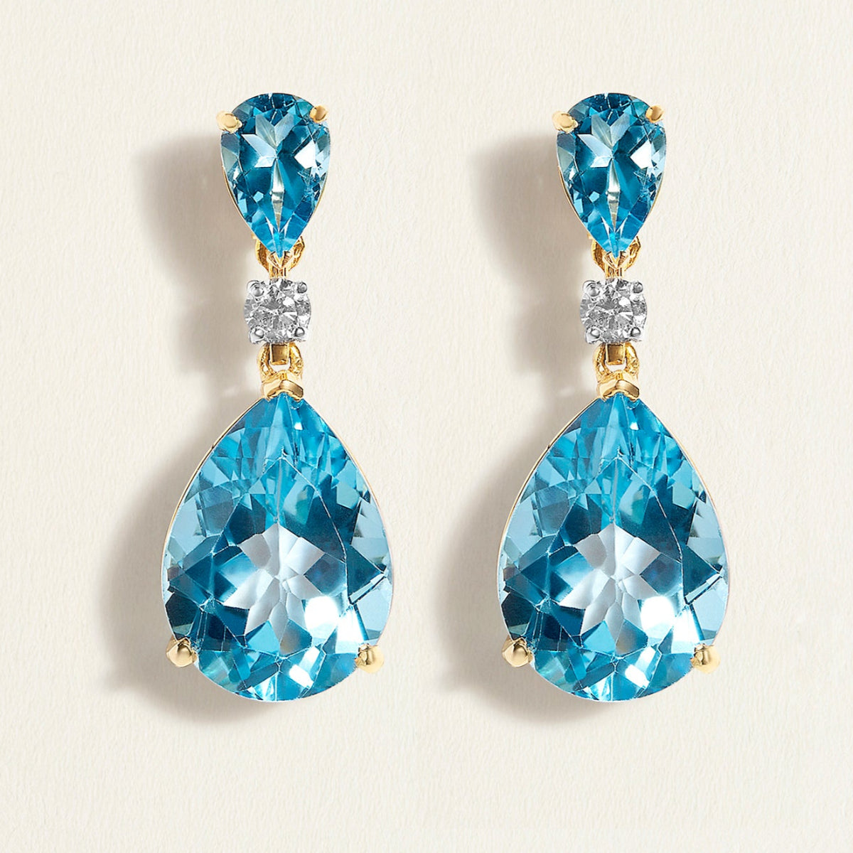 Pair of cocktail gold blue topaz teardrop earrings in gold on a light beige background