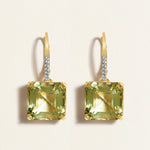 Pair of gold earring huggies with green asscher amethyst and diamonds gemstones on a beige background