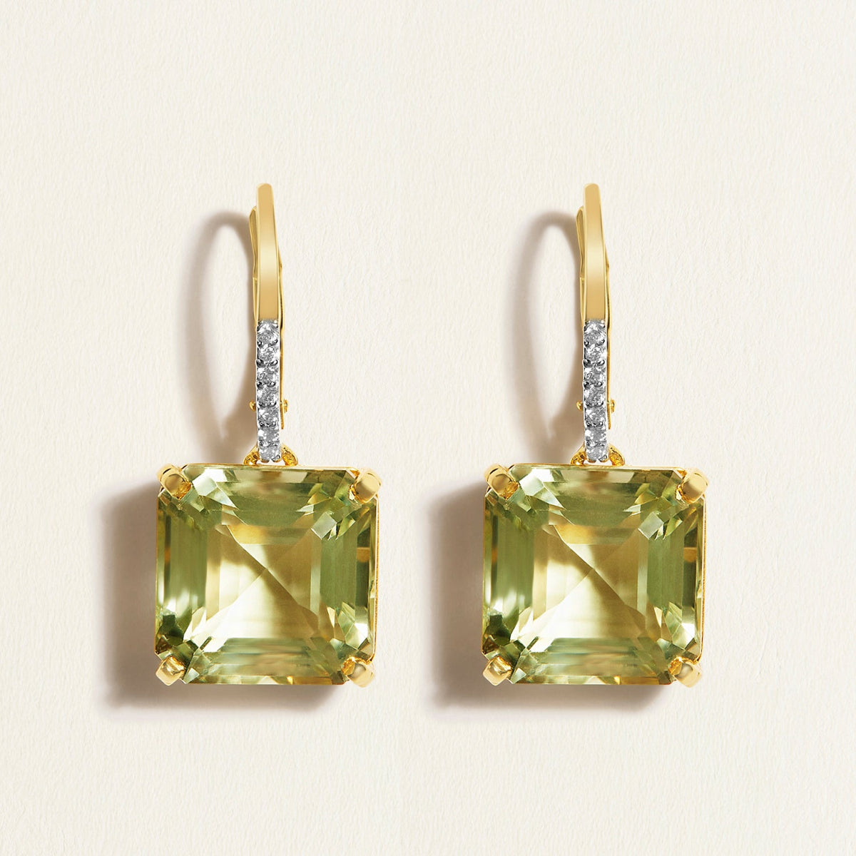 Pair of gold earring huggies with green asscher amethyst and diamonds gemstones on a beige background