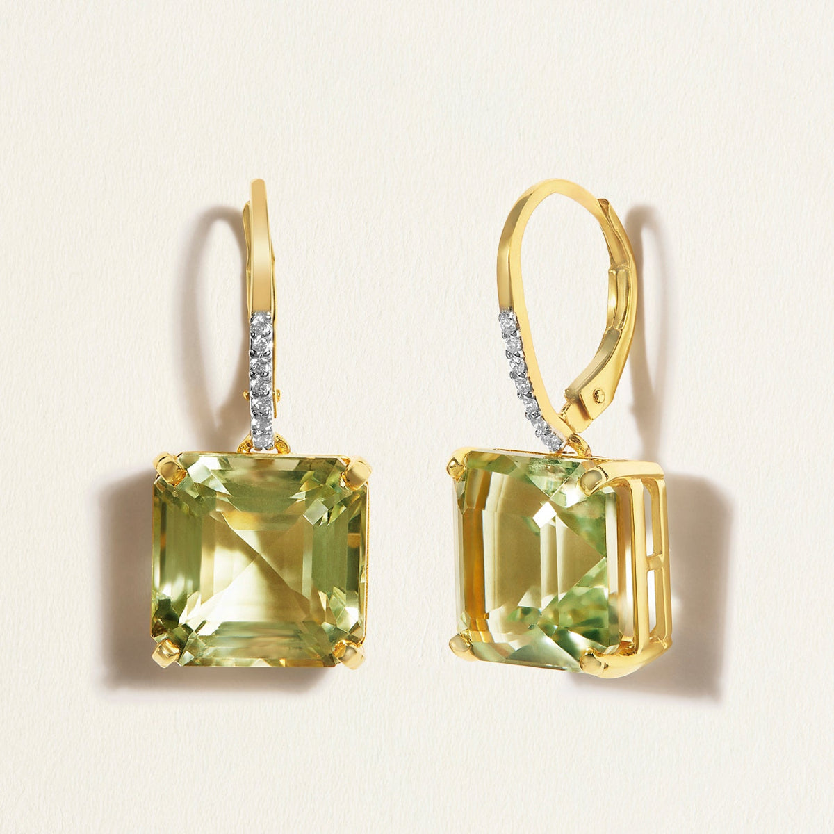 Gold huggies earrings with green amethyst gemstones on a light beige background
