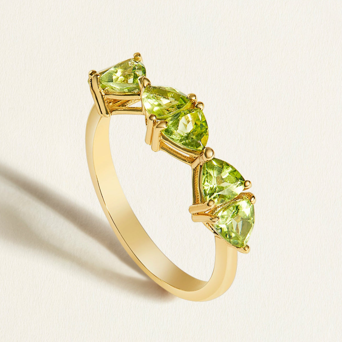 Gold stacking birthstone ring with green peridot gemstones on a light background