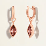Rose gold huggy earrings with marquise-shaped gemstones on a light beige background