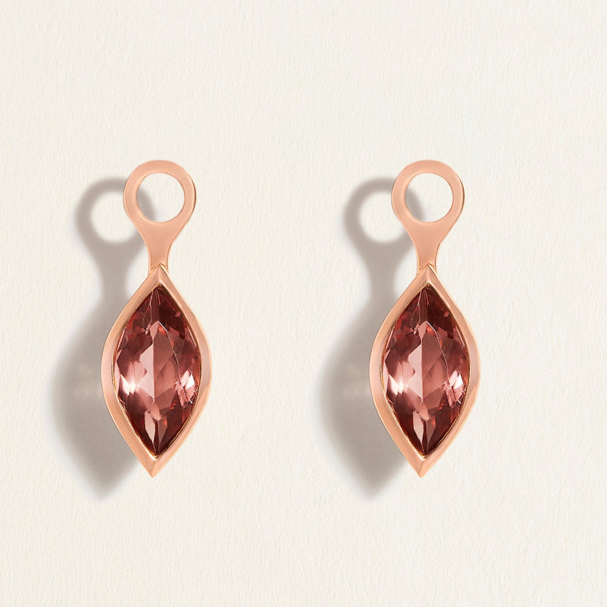 Rose gold earring charms with pink tourmalines gemstones on a light beige background