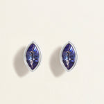 Pair of white gold earrings studs with blue tanzanites gemstones on a light beige background
