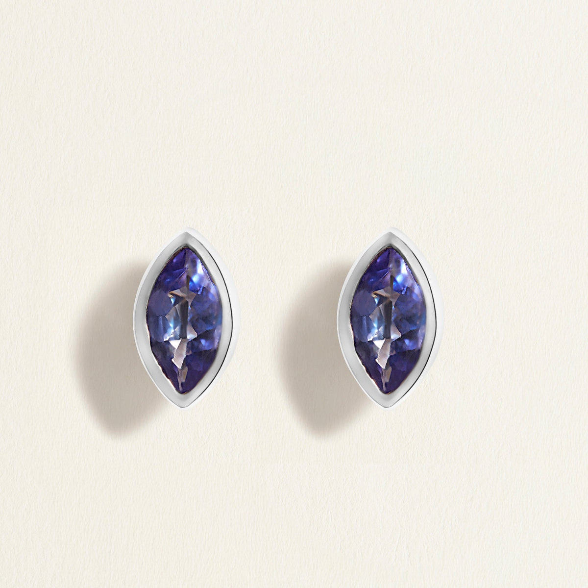 Pair of white gold earrings studs with blue tanzanites gemstones on a light beige background