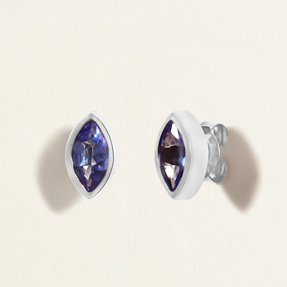 Pair of white gold earrings studs with blue tanzanites gemstones on a light beige background