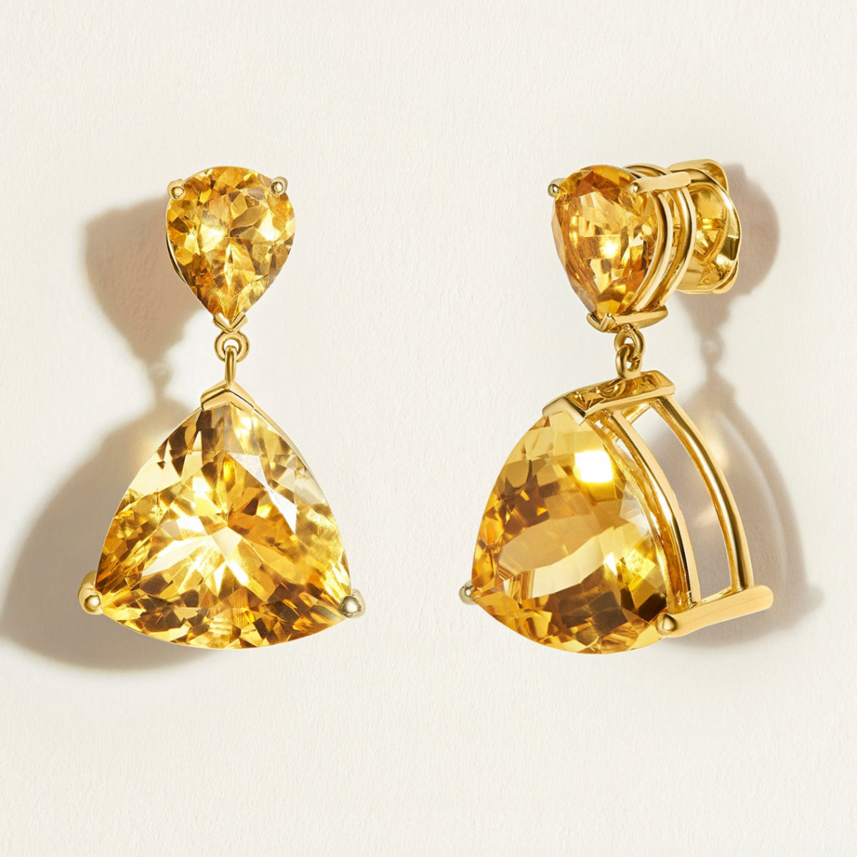 Pair of designer yellow citrine gemstone drop gold earrings on a light beige background