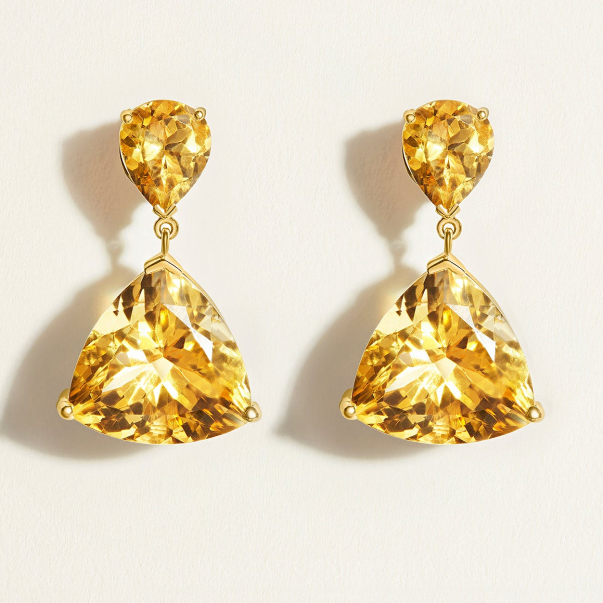 Pair of yellow citrine drop gemstone in gold earrings on a light beige background