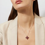 Woman wearing a gold chain necklace with a big 5 clover pink tourmaline pendant against a plain background