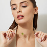 Woman wearing a gold chain with a green peridot large pendant against a plain background