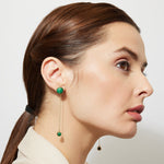 Woman wearing green malachite chain earrings against a plain background