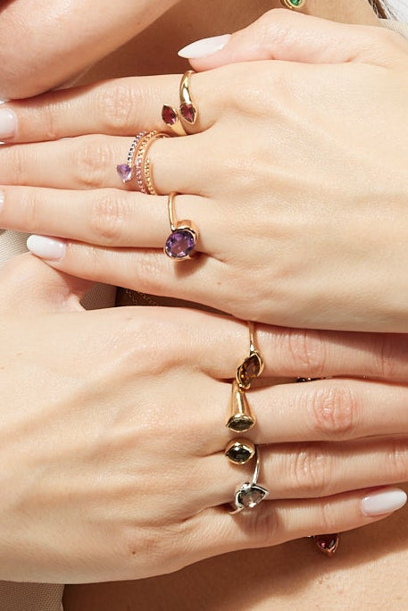 Woman wearing jewelry including earrings, rings, and a bracelet on a plain background