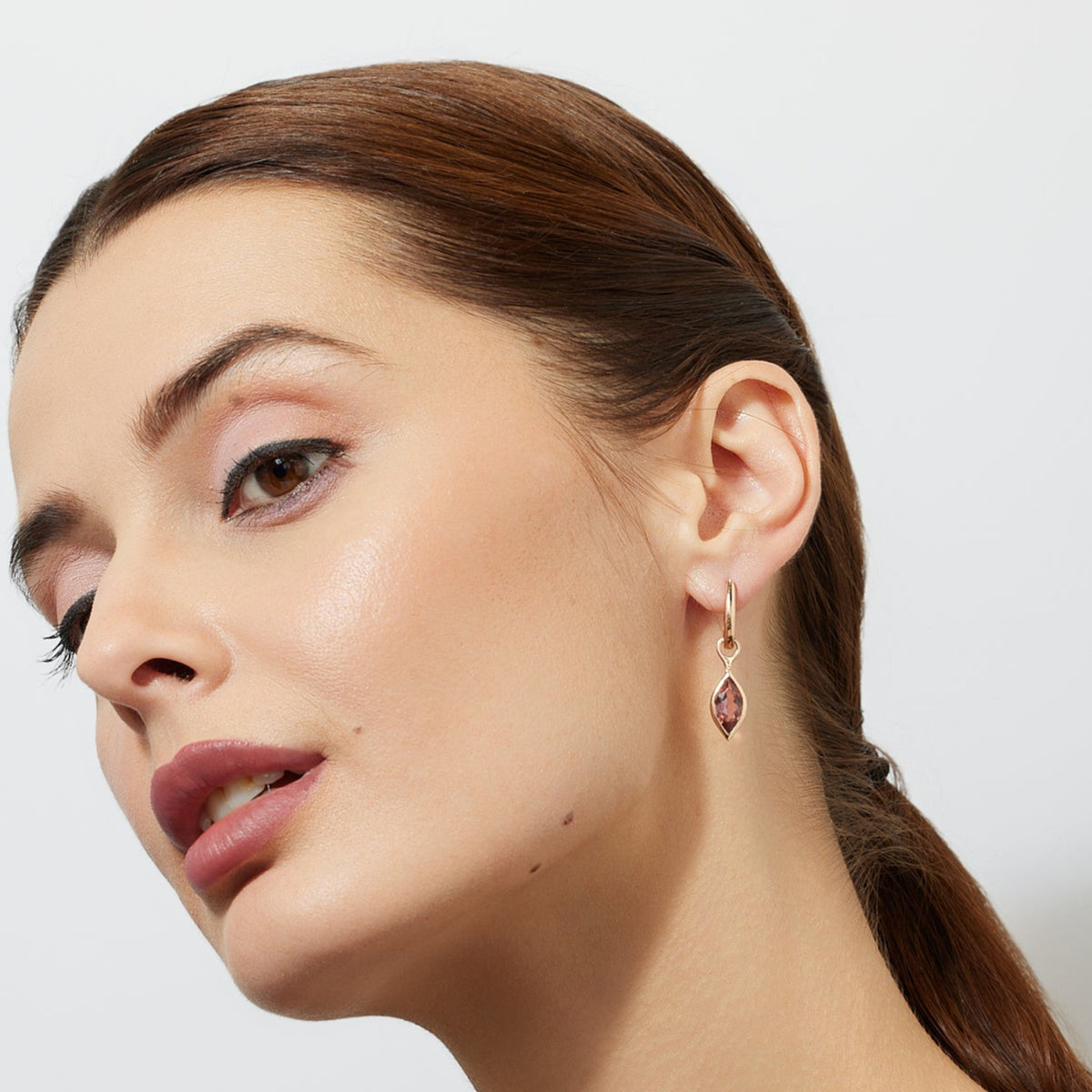 woman wearing a rose gold huggies earring with a marquise maroon tourmaline drop