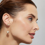 Close-up of a woman wearing opal with gold chain danglers earrings with a neutral background