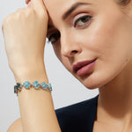 Woman wearing a clover pattern bracelet with blue topaz stones on a plain background