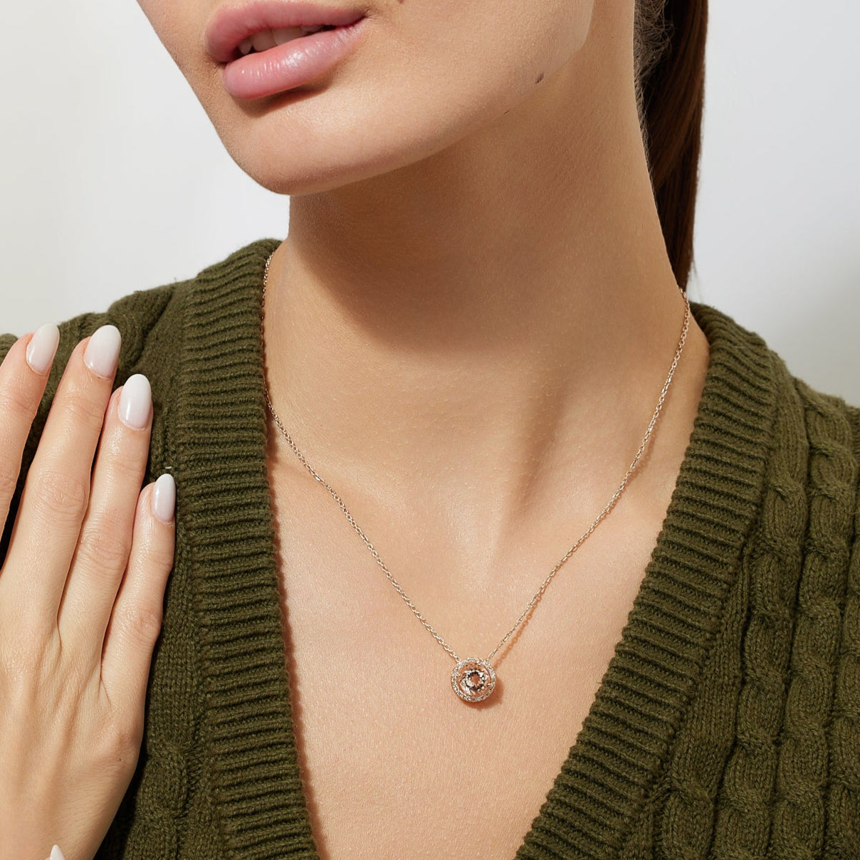 Woman wearing a gold chain necklace  with a round peach morganite pendant with diamond halo against a plain background