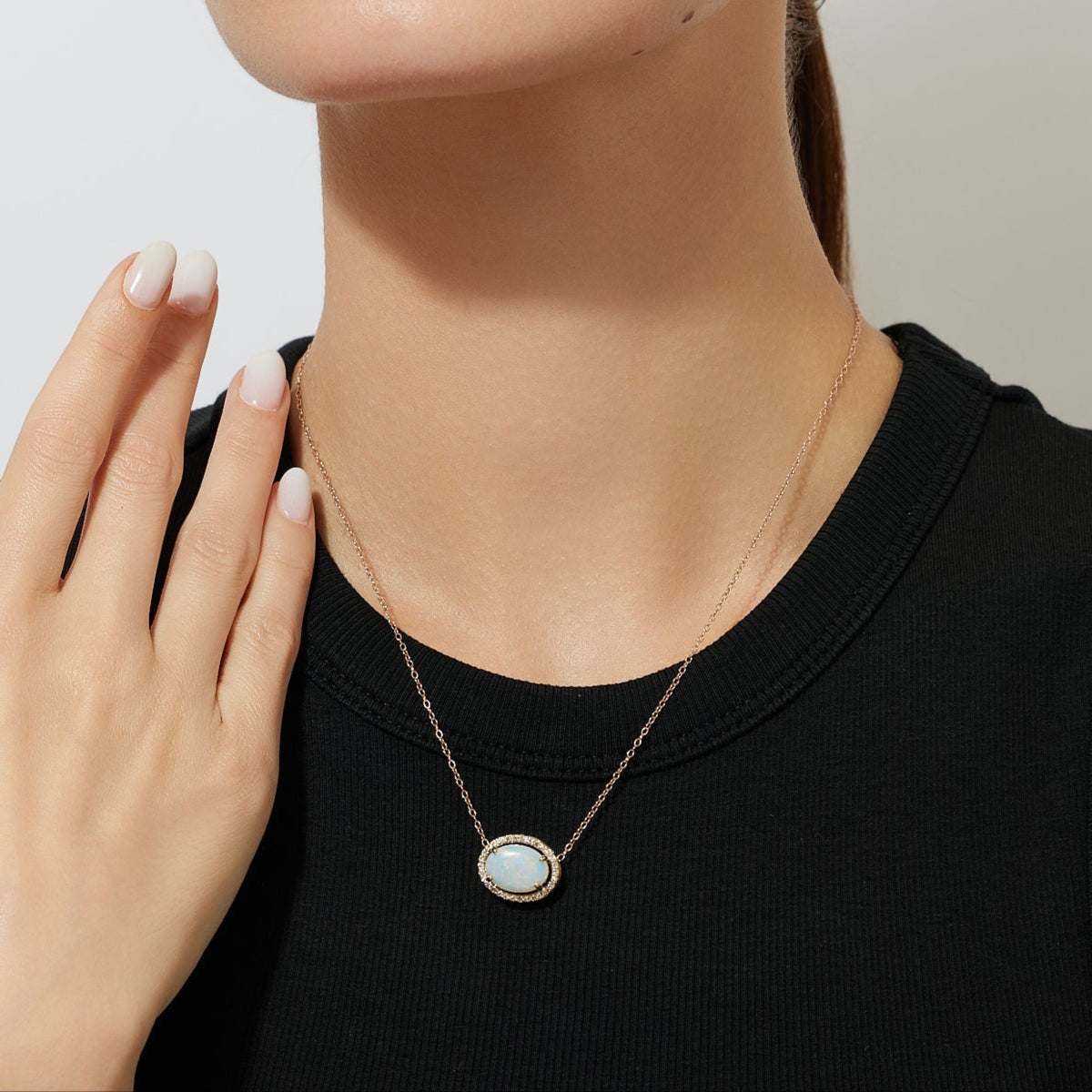 Woman wearing a gold chain necklace with a Australian opal diamond halo pendant against a plain background