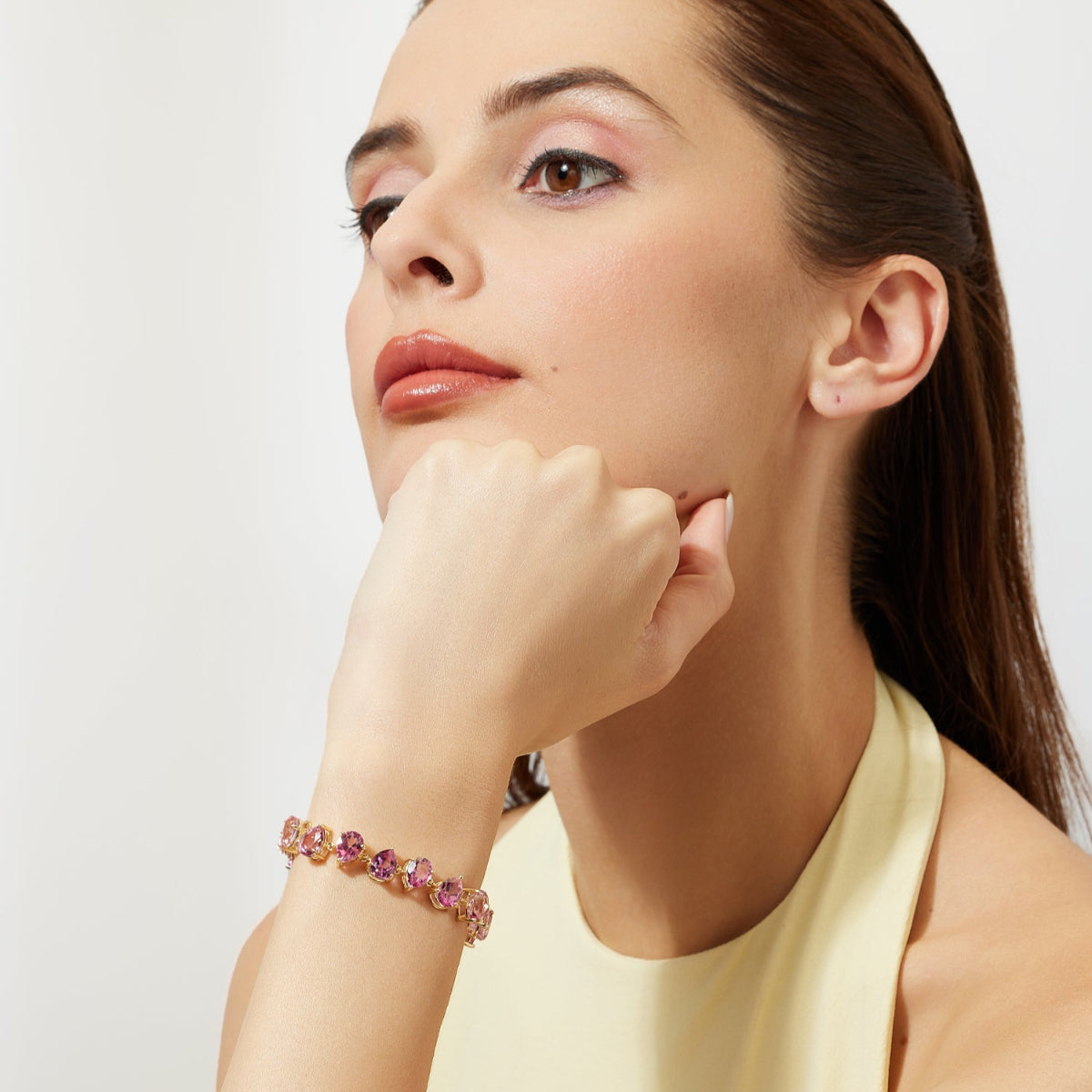 Woman wearing a gold bracelet with pink gemstones on a plain background